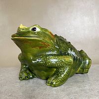 Full side view of green ceramic toad frog statue with textured surface and butterfly on nose