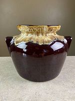 Photo of vintage stoneware crock with clear view of dark brown glaze and beige volcanic rim pattern, showing double handles on the sides and wide mouth.