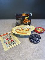 Photo of all items in lot including the Un-Candle flameless candle box, ceramic ashtray, black and white switchplate, two coasters, and pack of paper napkins.