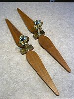 Pair of teak and brass wall sconce candle holders displayed on a light surface showing the side and angled views of the wooden and metal elements.