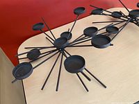 Two black metal starburst candle holders on a table, showing the top and side views of the circular candle platforms and radiating rods.