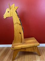 Side view of a large pine wood giraffe-shaped bench showing the giraffe profile with burlap mane and wooden handle on the neck.