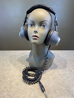 Front view of Realistic NOVA '30 headphones on display head, showing padded silver earcups and headband with coiled cable lying on surface.