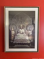 Black and white image of the Shaka Triad statues framed on a red wall, showing the statue details and frame edges.