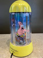 Photo of lamp side showing Patrick Star riding a bicycle inside clear yellow-topped and base lamp