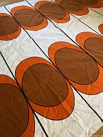 Close-up of fabric showing large brown circles inside orange rings on white cotton textile, highlighting pattern and condition.