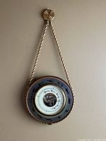 Full view of Zodiac barometer weather station hanging on wall, showing twisted cord and round instrument with zodiac signs around dial.