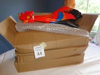 Three unopened cardboard boxes stacked with one rooster whirligig body visible on top wrapped in bubble wrap.