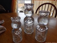 Three sculptured glass candleholders of varying heights resting on a wooden table with natural light from window