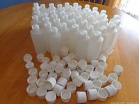 47 translucent plastic storage bottles arranged in rows with 54 white snap-top caps scattered in front, showing quantity and condition.