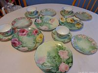Full view of all 4 place settings laid out showing cups, saucers, bread and butter plates, and luncheon plates with distinct floral patterns.