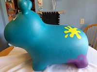 Blue rubber hippo-shaped bouncy toy with yellow and purple markings shown on a wooden surface.