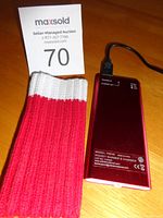 Full view of the hand warmer device next to a red and white knitted sleeve on a wooden surface with auction number card 70.