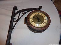 Side view of hanging clock and metal bracket showing ornate design and mounting arm