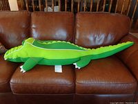 Side view of the large green alligator pool toy laid on a brown leather couch, showing body length and shape.