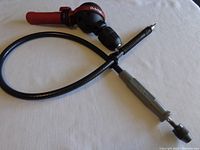 Shows both the Milescraft Orbiter drill attachment with red handle and the flexible drill extension attachment with coiled shaft and metal grip handle, laid on a white surface.