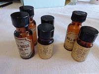 Six amber glass bottles on white cloth surface. Two Coty Wild Musk Oil bottles and four Village Bath Musk Oil bottles, two full and two partial.