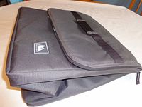Closed view showing the black cold food carrier with Arctic Zone logo patch on front and zipper top lid with handle.