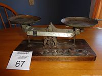 Front view of old balance scale showing two rusted metal pans on a wooden base with rusted metal frame and measuring bar.