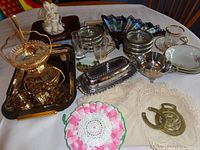 Wide view of assortment on table showing doilies, glass coasters, metal tray, fan, bowls, butter dish, napkin rings, figurine, and other items.
