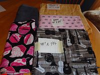 Four folded fabric pieces displaying different patterns and sizes on a table including cupcake, musical instruments, and crown motifs