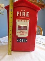 Front view of the red fire box landline phone with pull-down hook and 911 label with measuring tape showing approximately 14.5 inch height.