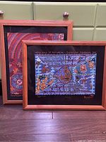 Two framed Australian Aboriginal art prints on fabric by Bulurru shown side by side. Frames are wooden with black mats.