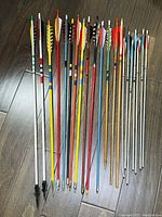 Photo showing a full set of 21 arrows laid out side by side, showcasing a variety of colors, fletching styles, and metal points.