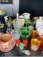 Wide view of assorted candle holders, vases, and decorative items on a black surface showing various colors, shapes, and materials including glass and ceramics.