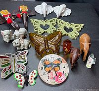 Overview of all elephant and butterfly decorative items including carved wood elephants, ceramic figurines, butterfly wall hangings, glass pig, and clock face.