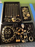 Overview of multiple gold tone chain necklaces with assorted pendants, a bracelet with rectangular segments, and various brooches with floral and animal designs.