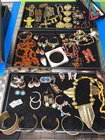 Full view of jewelry collection on black display trays showing earrings, necklaces, bracelets, rings and brooches of mixed materials and designs