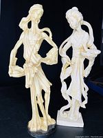 Photo showing both Asian statues—a male figure with baskets and a female figure with a basket and birds. Cream-colored with intricate hand carving.