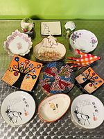 A full view of the assortment of small plates and ceramic items arranged on a green surface, including floral, mosaic, and animal designs.