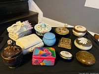 Photo of 12 assorted trinket jars and lidded decorative boxes on black surface next to stairs.