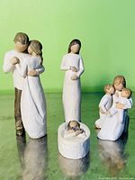 Wide shot showing all five Willow Tree figurines on a reflective surface with green background.