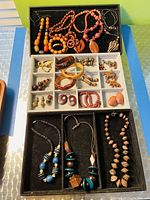 Wooden necklaces, bracelets, and earrings arranged on black trays showing variety and condition.