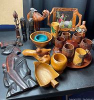 Photo showing entire wooden item lot including carved figurines, bowls, goblets, tray, decorative mug, and framed painting.