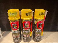 Photo showing three new cans of Great Stuff Big Gap Filler insulating foam with yellow caps and spray nozzles attached, placed side by side.