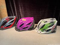 Three CCM brand kids helmets in black/red, purple, and white/green viewed from side on a surface