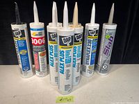 Photo shows nine tubes of caulking from brands DAP and Sila, all standing upright with labels visible. Various types and formulations are included.