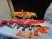 Four plastic toy air blaster guns displayed on a table including two large models and two smaller orange guns with tubes of foam darts