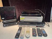 Full view of stacked DVD players, one VHS player, Bell branded devices and six remote controls in front.