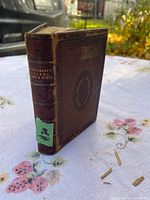 Antique leather-bound book with embossed cover and gilt title on spine sitting on a floral tablecloth.