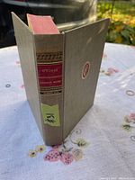 Side view of antique hardcover book with gray cover and red/gold label on spine showing title and author