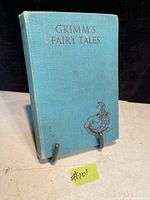 Front cover of the light blue hardcover book titled 'Grimm's Fairy Tales' with a small burgundy illustration on front and some light wear on edges.