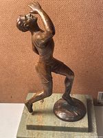 Side angle of bronze runner sculpture showing profile and muscle detail on marble base.