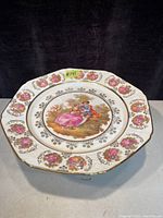 Top view of one compote showing octagonal shape, central pastoral scene with couple, surrounding pink rose medallions and gold trim.