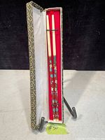 Set of three decorated chopsticks in a fitted box with red velvet lining and patterned exterior.