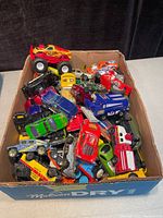 Box of assorted die cast toy trucks and cars including Hot Wheels, Matchbox, and Maisto brands in various colors and styles.